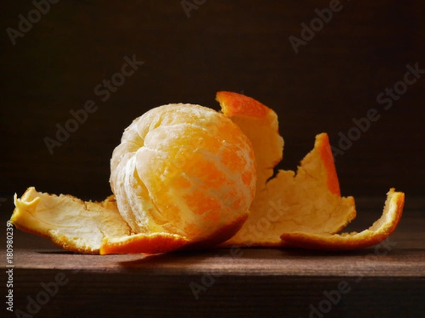 Obraz Peeled mandarin on a wooden dark background. Fruit of tangerine without skin. Soft side light on the dark. Healthy eating concept, vegetarian, vegetable healthy food.
