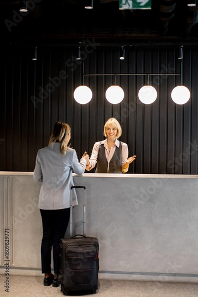 Fototapeta Friendly hotel receptionist welcoming a guest at the front desk during the day