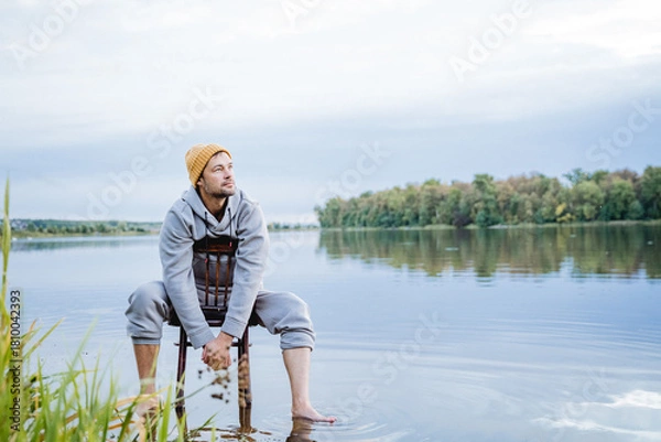 Fototapeta man enjoying peaceful water view, individual dressed casually experiencing calmness near serene water body, person in relaxed clothing immersing in quiet and peaceful lakeside environment