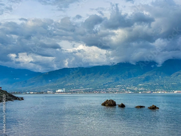 Fototapeta Dramatic clouds hover over tranquil blue water and mountains, a peaceful palu city beckons in the distance