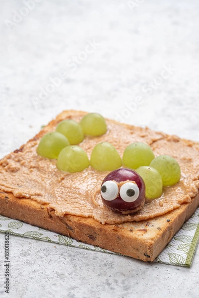 Fototapeta Creative snack idea with peanut butter and grapes shaped like a caterpillar on toasted bread