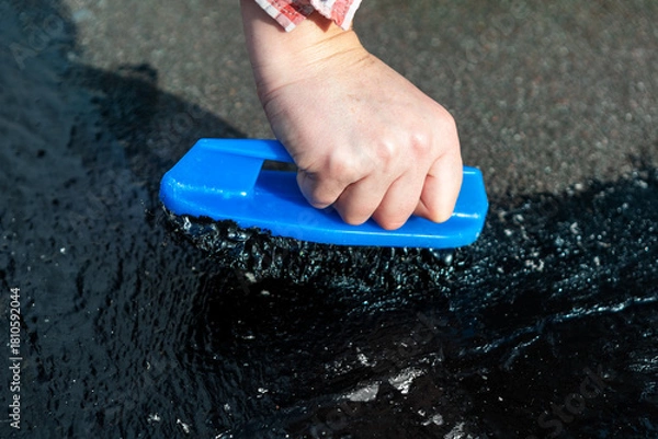 Obraz Hand pushes brush through thick black sealant, applying waterproof coating to surface like roof or pavement. Process involves using asphalt or tar compound with mastic brush for sealing and repairing