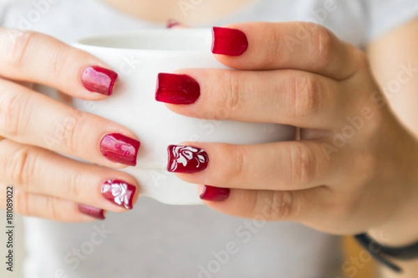 Fototapeta Woman's elegant red manicure and cup of green tea with lemon in cafe.