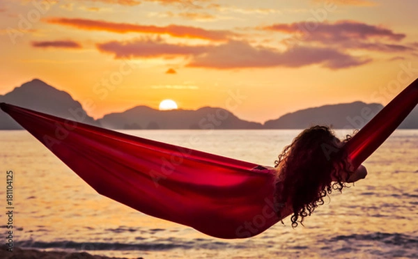 Obraz Curly young woman relaxing in a red hammock on a tropical island enjoying the sunset