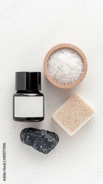 Fototapeta A flat lay composition of spa and wellness items including a black stone, bath salts in a wooden bowl, a pumice stone, and a dark bottle with a blank label.
