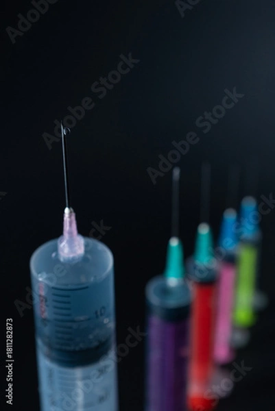Fototapeta Sharp Focus on Syringe Needle Tip with Fluid Drop. A composition of various size syringes on a dark background, highlighting themes of measurement, vaccination, and lab work.