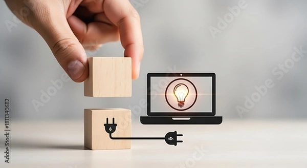 Fototapeta Hand placing a wooden block to complete a connection between a laptop with a lightbulb icon and a power plug, symbolizing innovation and ideas