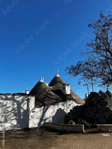 Fototapeta Trullo Architecture: A picturesque scene of traditional Trullo architecture bathed in the bright sunlight, with their characteristic conical roofs reaching towards a vibrant blue sky.