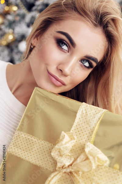 Obraz beautiful girl with blond hair in cozy clothes posing near New Year tree with presents