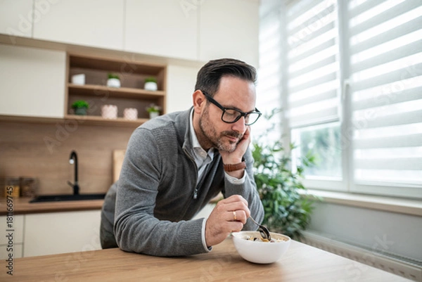 Obraz Man contemplating while eating breakfast cereal in kitchen