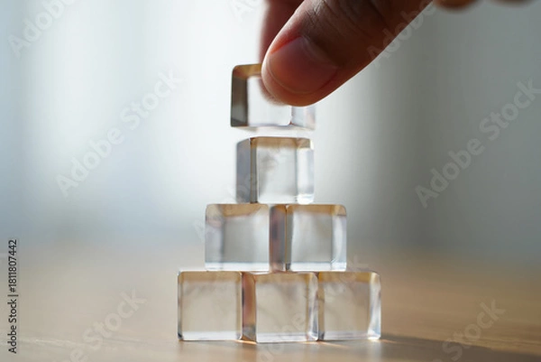 Obraz Hand Places Clear Acrylic Cubes in Pyramid Shape for Construction Building or Strength Concept 150 Characters