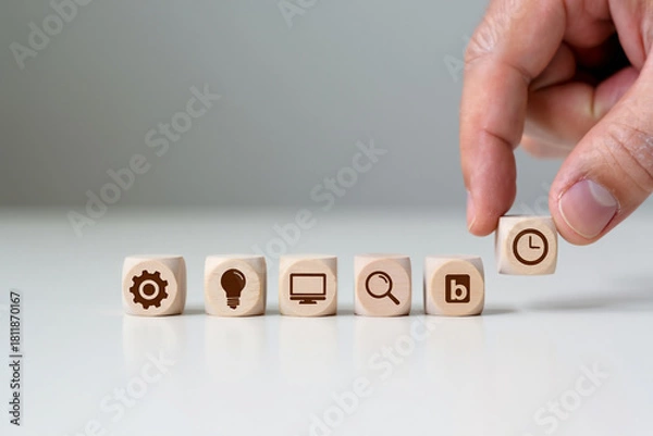 Fototapeta Hand Placing Wooden Cube with Clock Icon on Row of Other Cubes with Gear Bulb Computer Magnifier Blog Symbols on Table Concept