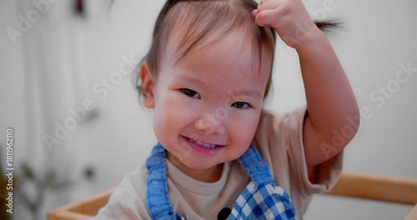Fototapeta Cute Asian toddler smiling and looking at camera, wearing a blue checkered apron, creating a joyful and playful atmosphere.