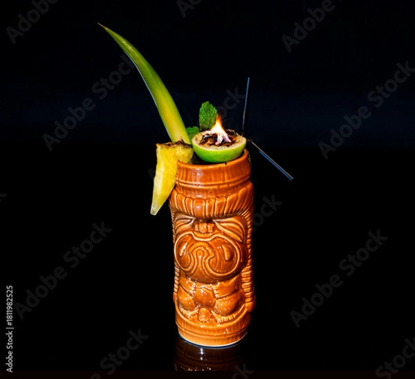 Fototapeta Dramatic Flaming Tiki Cocktail in Ceramic Mug with Pineapple Garnish on Black Background