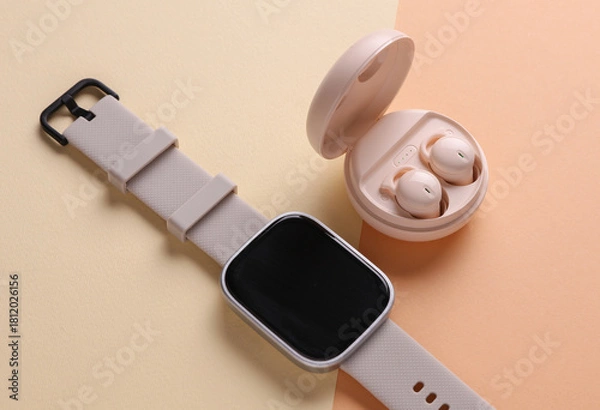 Fototapeta Modern Wireless Bluetooth Earbuds with Charging Case and smart watch on Beige Background. Top view. Flat lay