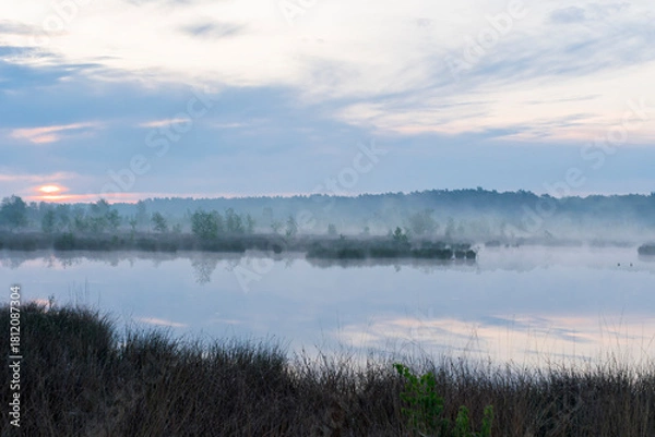 Obraz In the early morning a lake with a reflection of the sky. The sky is overcast and the air is cool and damp. The scene is quiet and peaceful, with the lake providing a sense of solitude and calm. Dwing
