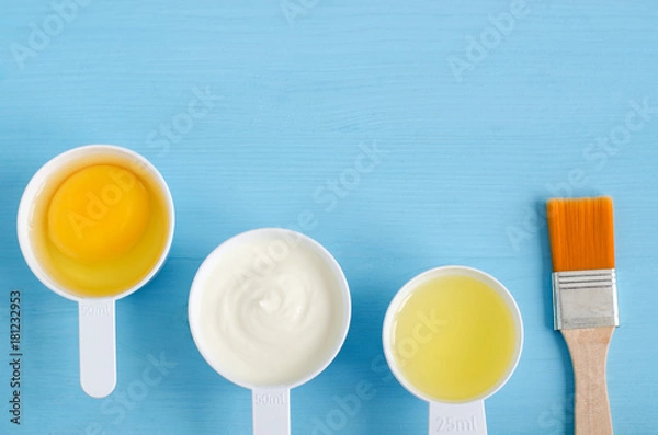 Fototapeta Sour cream (greek yogurt), raw egg and olive oil in a small plastic scoops - ingredients for preparing diy masks, scrubs and moisturizers. Homemade cosmetics. Top view, copy space.
