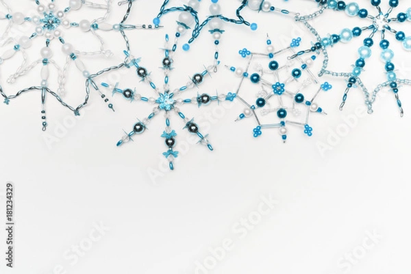Fototapeta Christmas or winter concept. Border of various handmade blue snowflakes made from beads and bugle on white desk background, top view. Layout for greeting card and winter holidays