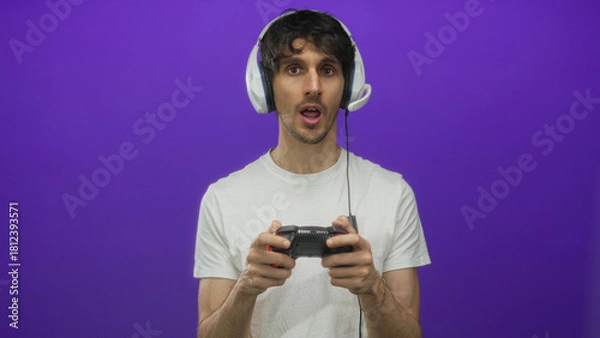 Obraz Man wearing headphones holding game controller and pressing buttons in purple studio setting; concentration.