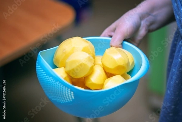 Fototapeta Woman's hand carrying a blue plastic bowl filled with peeled potatoes