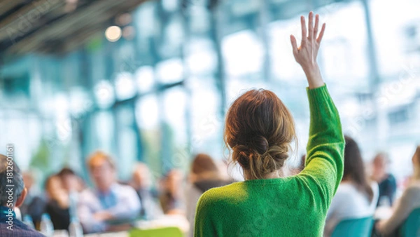 Fototapeta Woman in green sweater raises hand during a conference, actively participating in a group discussion or Q&A session.