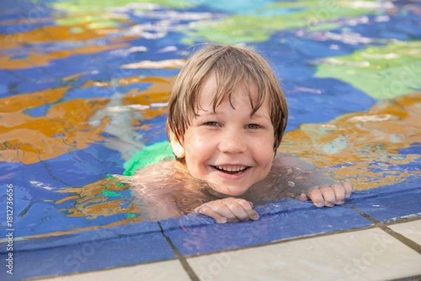 Fototapeta Smiling boy enjoying time in an outdoor swimming pool, holding onto the pool edge on a sunny day. Summer vacation and fun water activities for kids.