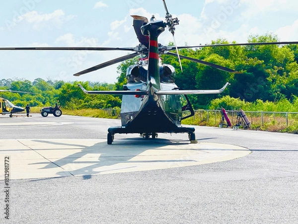 Fototapeta Helicopter Parked on Helipad with Green Forest Background
