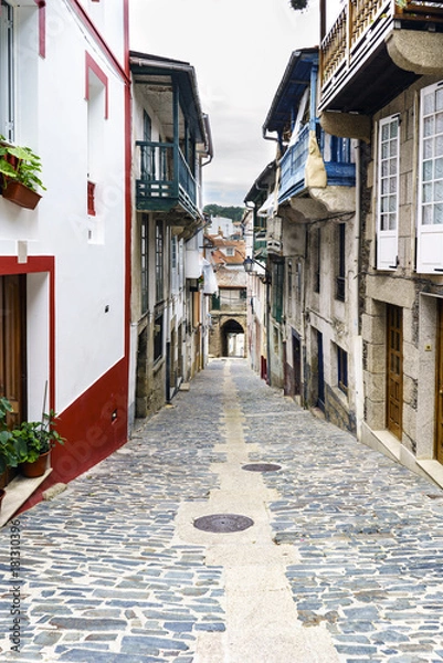 Fototapeta Typical street of a village of galicia on slope and finished in an arch with the stone floor and old houses in a village called Betanzos in Galicia, Spain