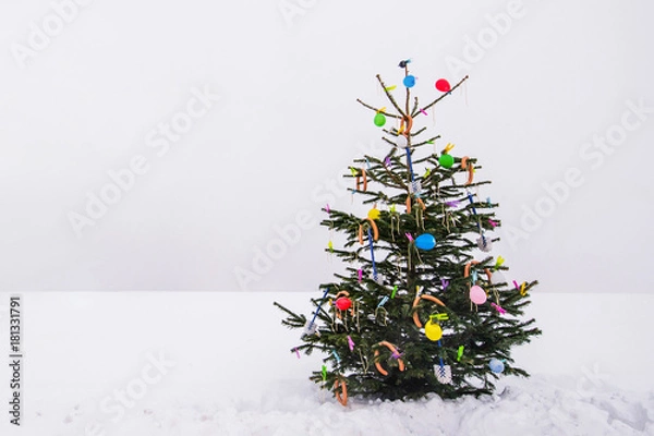 Fototapeta curious open air christmas tree in the snow decorated with sausages, balloons, toilet brushes and clothespins
