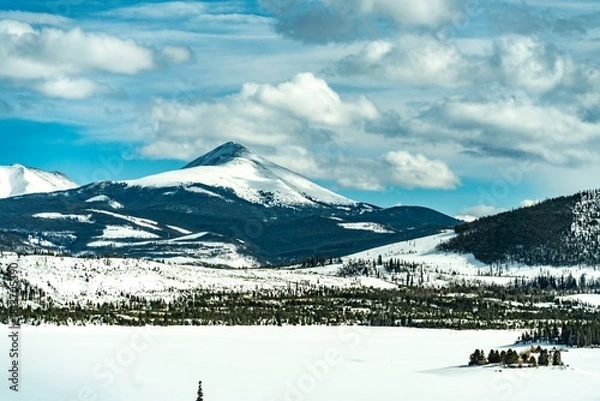 Fototapeta Scenic winter landscape featuring snow-covered mountains and frozen lake under a cloudy sky in a remote natural area