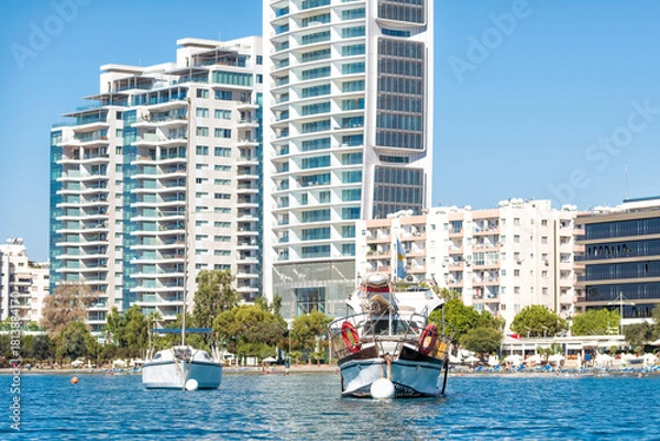 Fototapeta Two boats floating on water with modern apartment buildings in the background in Limassol, Cyprus