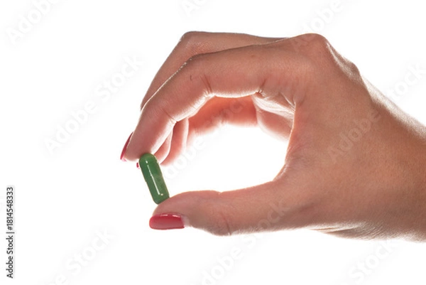 Obraz Backlit close-up of a female hand holding a green pill. Artistic silhouette lighting suitable for beauty supplements and women's health topics.