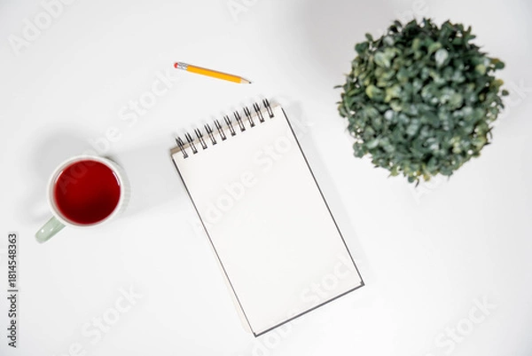 Obraz Clean, minimalist workspace with a blank spiral notepad, red tea, and green plant. A versatile background for education, business, or personal to-do lists.