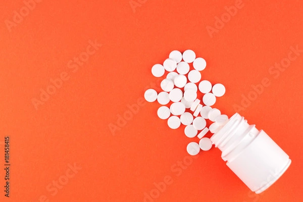 Fototapeta Close up white pill bottle with spilled out pills on orange background with copy space. Focus on foreground, soft bokeh. Pharmacy drugstore concept. Top view