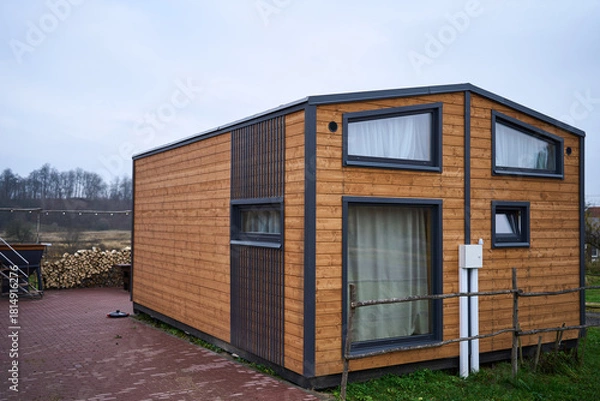 Obraz modern wooden tiny house exterior with windows, timber cladding and sleek frames on paved lot, compact modular