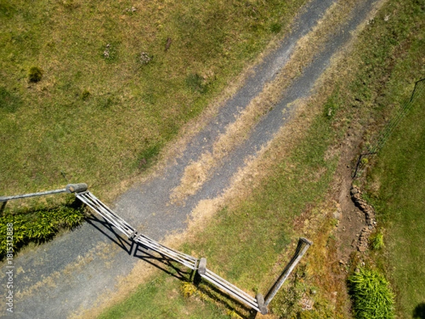 Fototapeta Aerial view of rural farm gate and gravel driveway in open green countryside