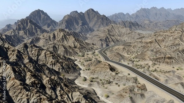 Fototapeta An aerial view of a road winding through a barren, mountainous desert landscape under a clear sky