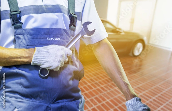 Obraz Hand of car mechanic with wrench with blurred Auto repair garage on background.	