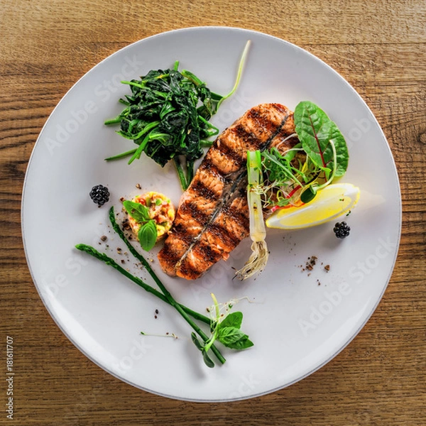 Obraz Salmon fish stake cooked on a grill with healthy salad on a plate. Healthy food made of fish and vegetables on a table. Top view.