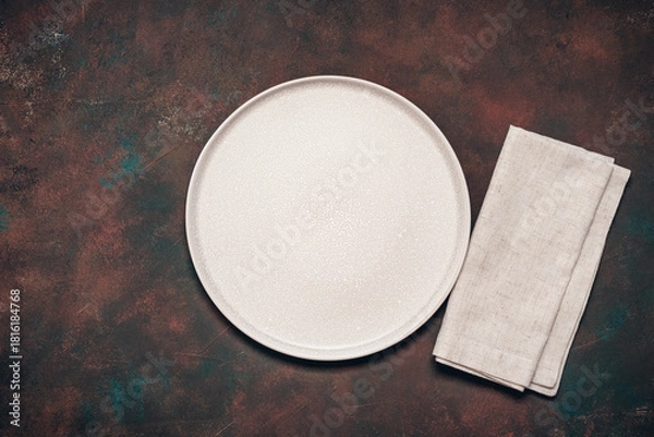 Fototapeta Empty beige plate and linen napkin on dark rusty grunge background, top view, flat lay, copy space.