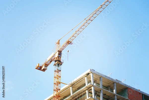 Fototapeta A tall crane is building a tall skyscraper to the very clouds