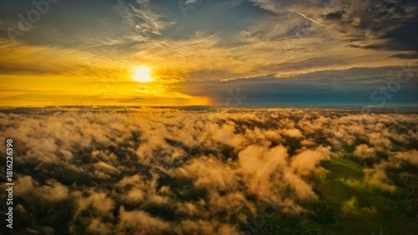 Obraz A high-altitude aerial photograph capturing a sunrise above a vast forest with golden morning mist drifting through the treetops
