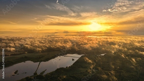 Fototapeta A high-altitude aerial photograph capturing a sunrise above a vast forest with golden morning mist drifting through the treetops