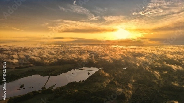 Fototapeta A high-altitude aerial photograph capturing a sunrise above a vast forest with golden morning mist drifting through the treetops