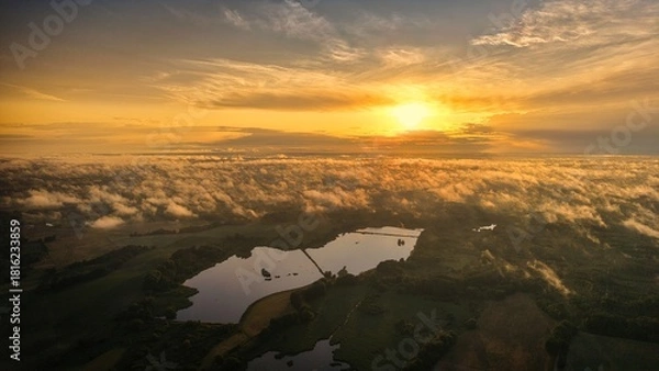 Fototapeta A high-altitude aerial photograph capturing a sunrise above a vast forest with golden morning mist drifting through the treetops