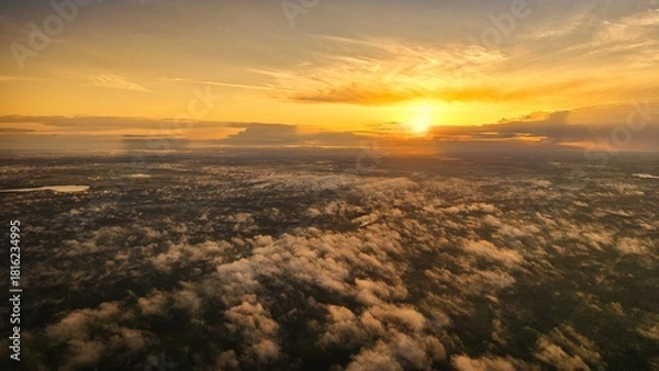 Fototapeta A high-altitude aerial photograph capturing a sunrise above a vast forest with golden morning mist drifting through the treetops