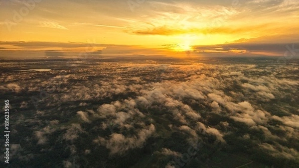 Fototapeta A high-altitude aerial photograph capturing a sunrise above a vast forest with golden morning mist drifting through the treetops