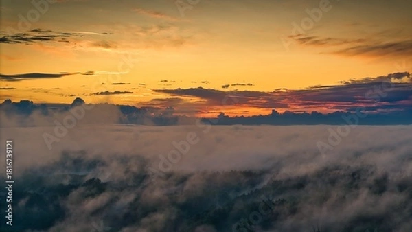 Fototapeta A high-altitude aerial photograph capturing a sunrise above a vast forest with golden morning mist drifting through the treetops