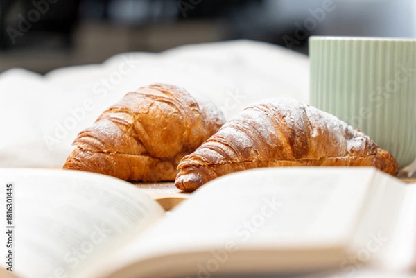 Fototapeta Eye-level view of sugar-dusted croissants and an open book, capturing the essence of a lazy weekend morning.