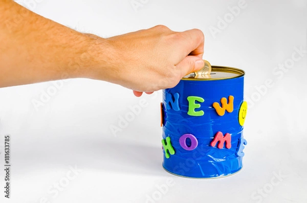 Fototapeta A person adding a coin to a handmade money box with New home inscription on a white background